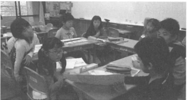 図 8 学習机での活動 ( 3 人の視線が外れている） 4 .  授業の考察 4 .   1 .  共通テーマがもたらす効果 図 7 の板書記録を見ると，特に， 2 年生の発言にあ った「お客さんへのサービス」が， 1 年生の家族への サービスヘとつながった）この瞬間から， 1 年生は， 意識を向けていたお手伝いから，なにかサービスをあ げられることはないかと考えるようになっ t 4 行動だ けではない，手紙やその内容から読み取れる「気持ち」 が生み出す笑顔について考えていたからと察する。 1 年生は，サー
