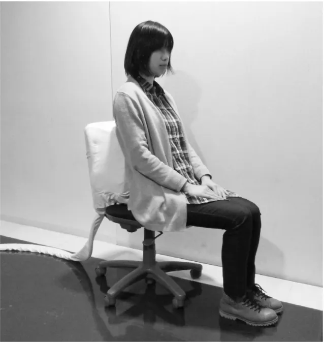 図 3.1 椅子型システム Breath Chair を使用している様子 3.2.  システム構成  本システムは，密閉したウレタンスポンジを椅子の背もたれに内蔵している．ウレタン スポンジに対し，真空圧で圧縮および非圧縮を繰り返し行い，その体積変化によって，人 間の呼吸時における胸郭の動きを疑似的に提示する．これにより身体接触しているかのよ うな感覚を与え，恐怖や不安の軽減を狙う．本システムの構成を図 3.2 に示す．密閉したウ レタンスポンジから，真空ポンプ（ ULVAC 製   DA-60S ）によっ