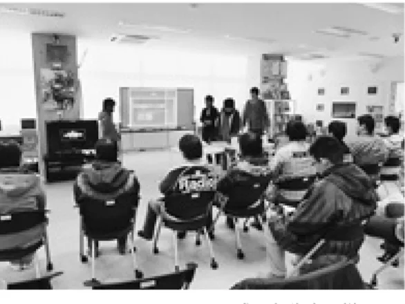 図 チーム No．の作品の シーン 図 チーム NO．による撮影の様子 図 チーム NO．による成果報告会の様子 図 チーム NO．の作品の シーン替え，より分かり易く，よりメッセージ性が高まるように制作している。図 に制作したCMの シーンを，図 にその撮影の様子を示す。さらに，学生たちは，課題を整理し，具体的にどう工夫し，どのような点で苦労したか，どのように課題を克服したのかをスライドに整理し，図 に示すように納品後に成果報告を行った。）プロジェクトチーム No．による「自転車の右側通行」第 チームは，
