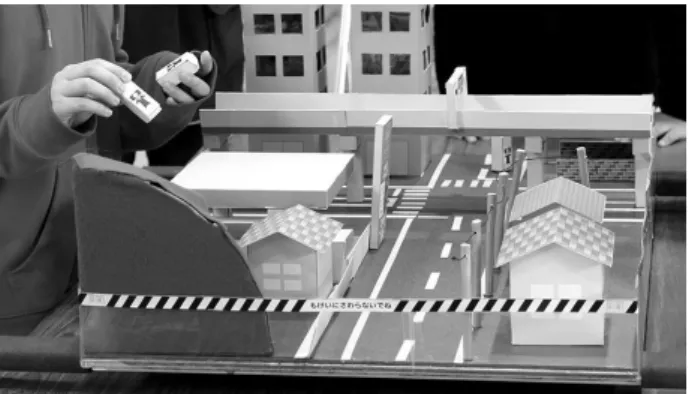 図 10  子ども達自身で揺らすことが可能な街の模型  図 11  高速道路の模型  図 12  電柱の模型    また，モデルコンテンツとデジタルコンテンツをつなぐ役 割として「キャメラ君」というキャラクターが設定されてお り，街の模型の中で地震によって危険なことが起こりそうな 箇所に子ども達自身が設置できるようになっている．キャメ ラ君は撮影をするという設定となっており，キャメラ君の視 点から街を撮影するという役割が与えられている（図 13） ． 図 1  モデルとデジタルコンテンツの橋渡しをするキャメ