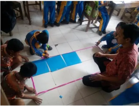 Gambar 1. Guru menyajikan ubin pada lantai yang telah diberi kertas warna 