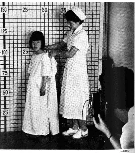 FIGURE 5: Young survivor being measured by a kindly nurse133