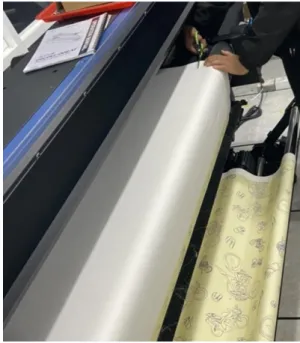 圖 2-17 剪刀裁剪。  2-4-2 固色機機台操作：  1.  將印好的布裁剪下來後，等待固色機升溫到 140 o C 到 150 o C，就可 以把布架上去固色，轉速調整到 0.22 rpm，溫度為 150 o C。先拿導 布當作前頭引導，利用針線或訂書機把兩塊布連接在一起餵入，如 圖 2-18 及 2-19。  圖 2-18  連接印花導布與印花布。 